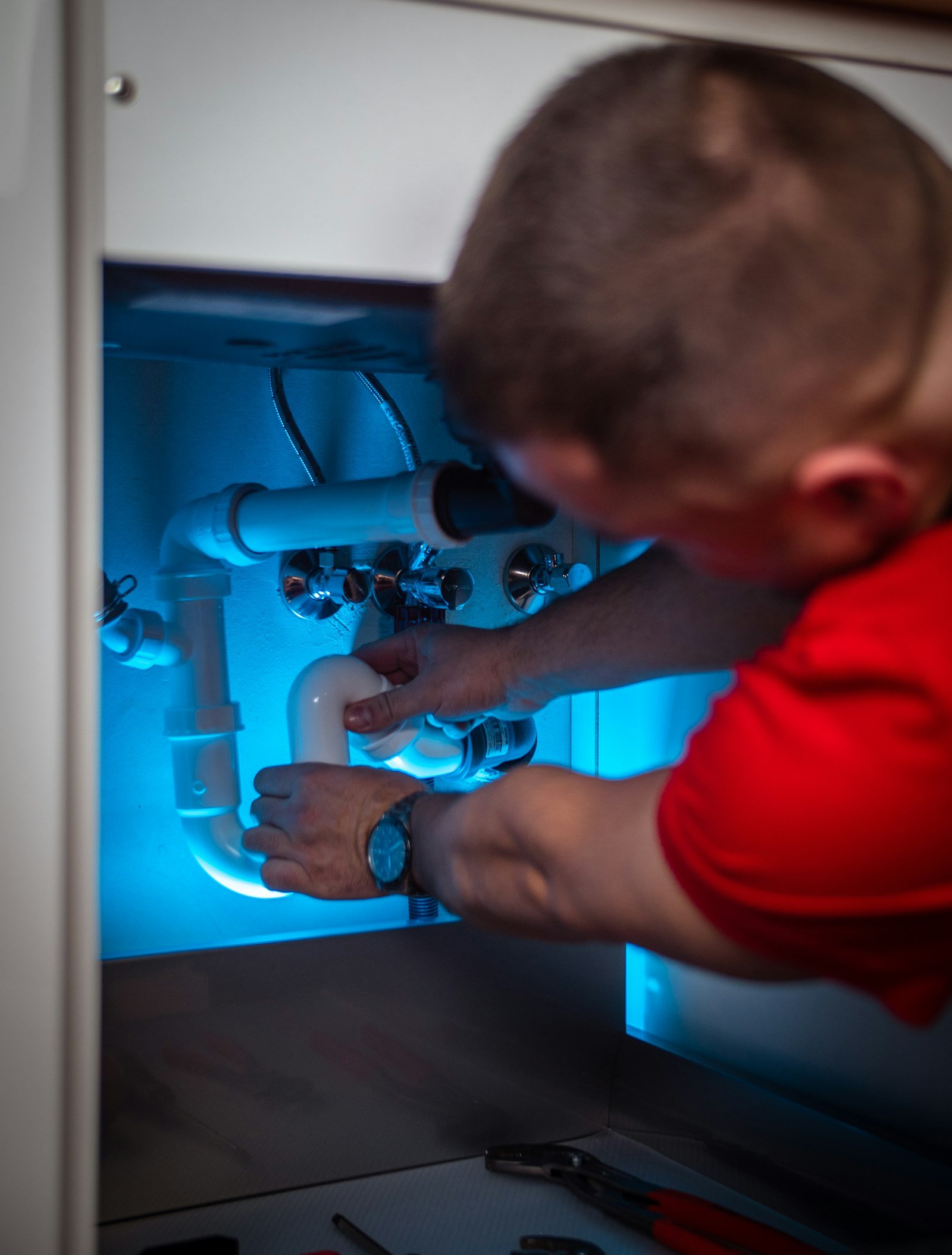 Technician repairing a leaking supply line inside an under-sink cabinet